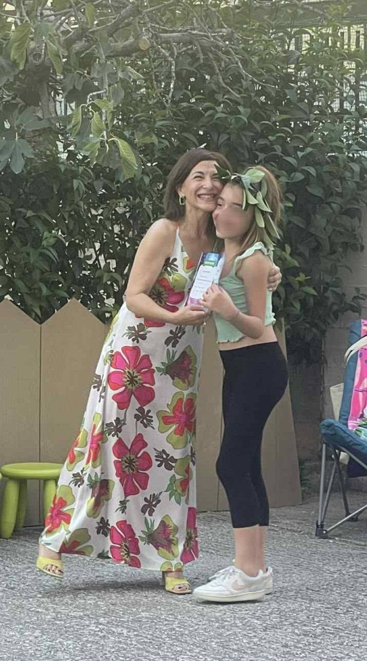 Εκπαιδευτικός αγκαλιάζει μαθήτρια μπροστά στο σκηνικό της γιορτής.