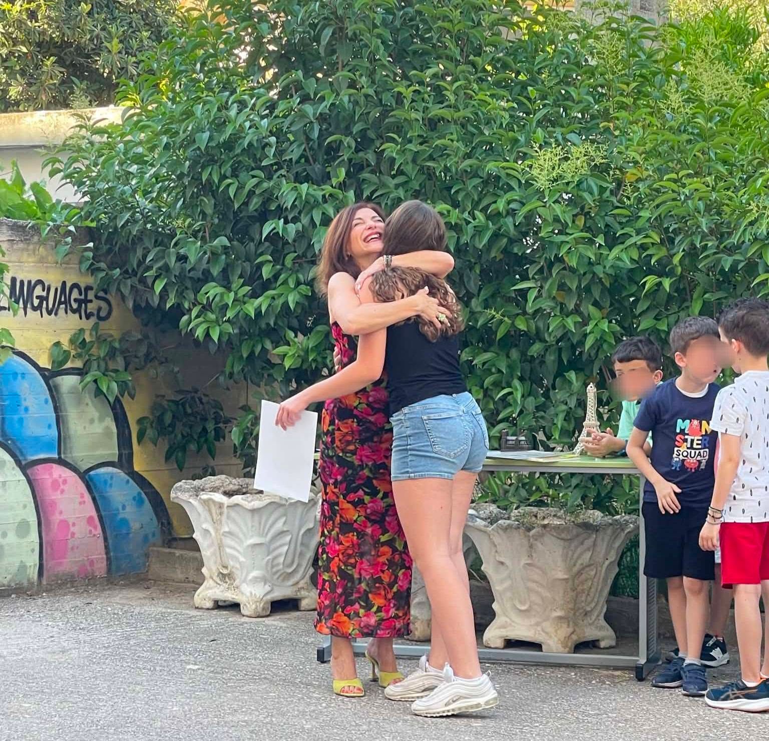 Εκπαιδευτικός αγκαλιάζει μαθήτρια στο προαύλιο.